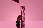 Liquid collagen dripping from a sachet with berries on a reflective pink surface, showcasing Calmerceuticals product.