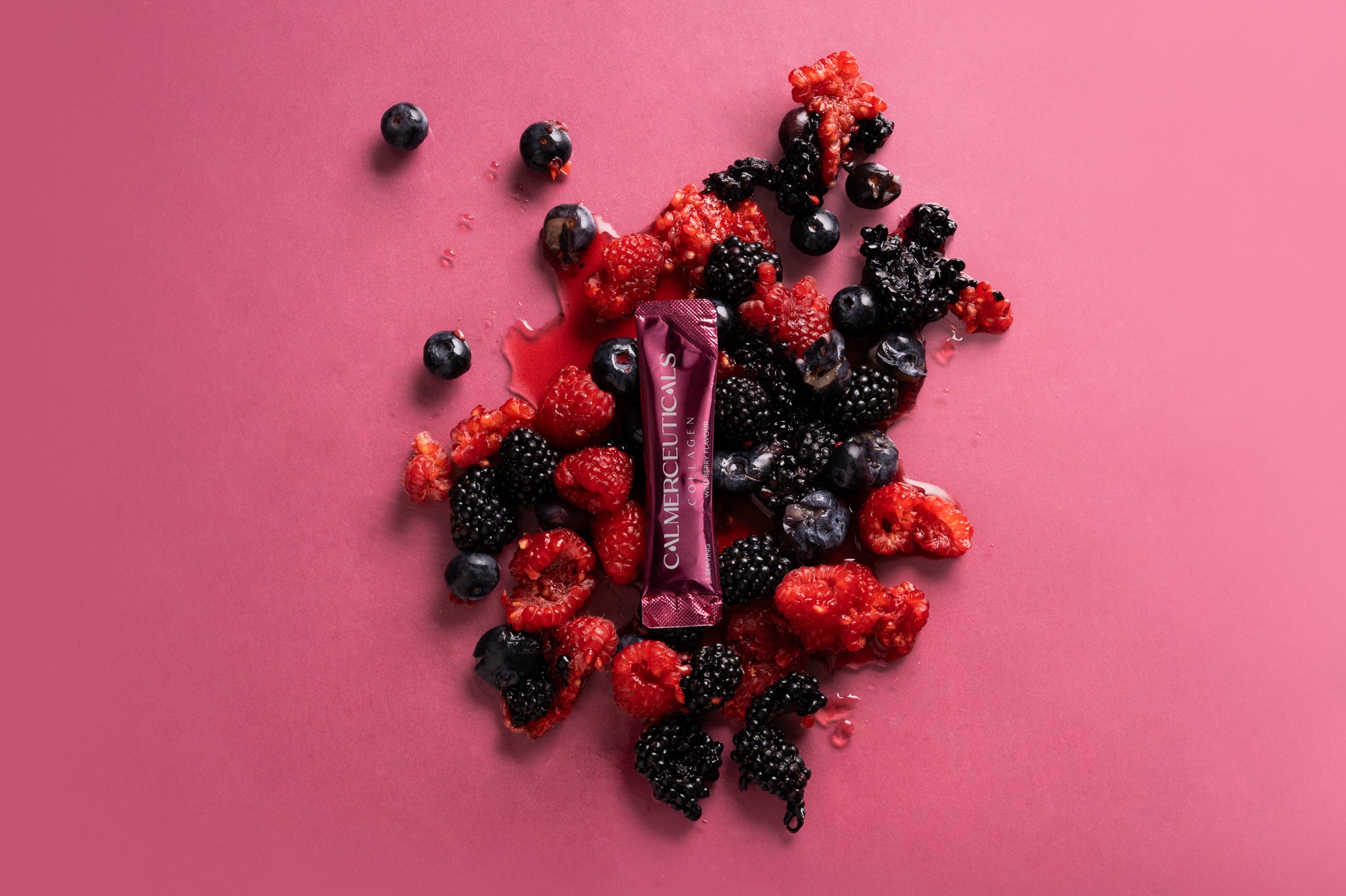 Colorful assortment of berries with a Calmerceuticals liquid collagen stick on a pink background.
