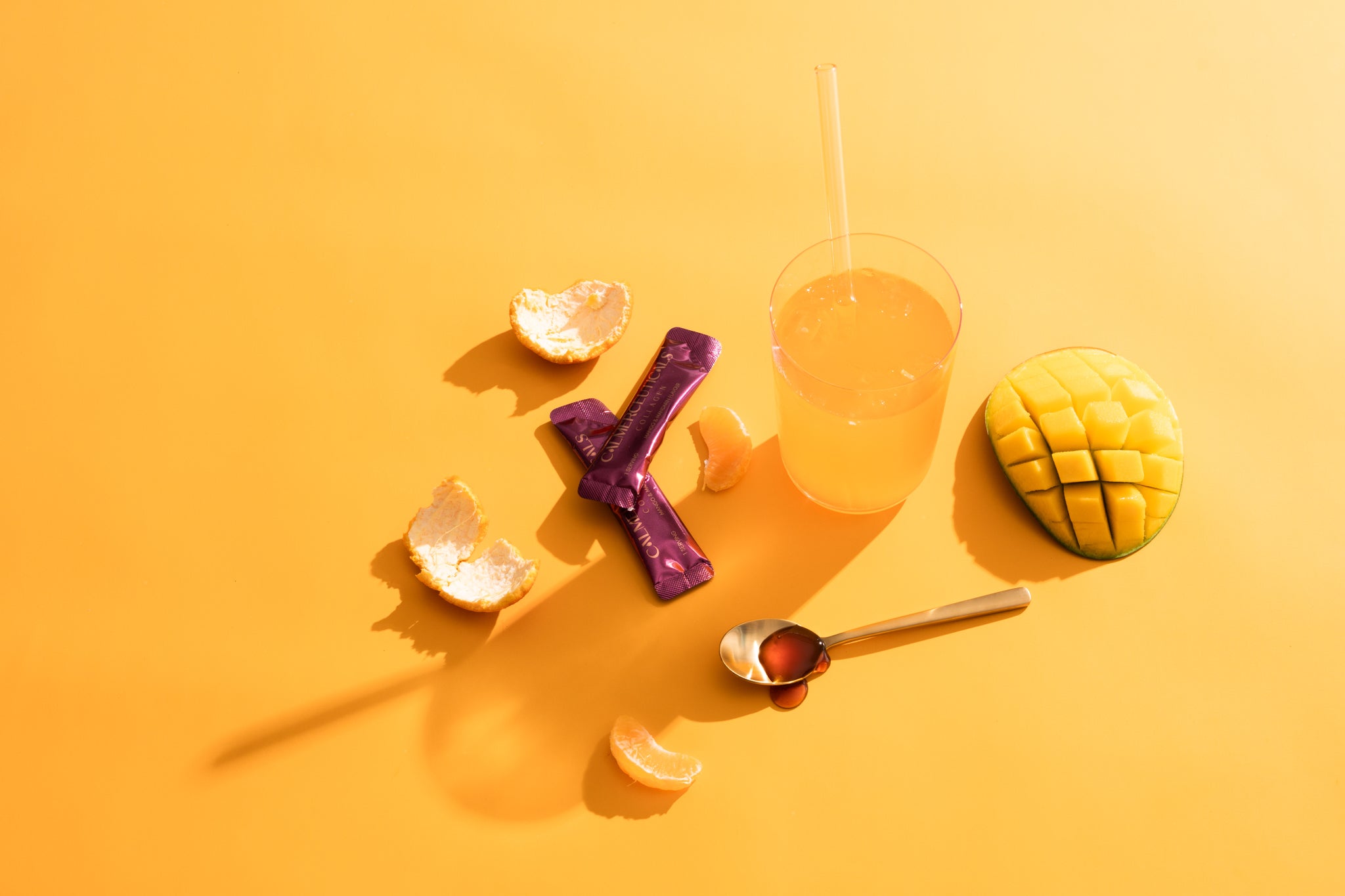 Colorful snacks and a drink on a yellow background, featuring mango, mandarin, and a purple candy bar.