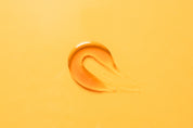 Drop of liquid collagen on a vibrant yellow surface, showcasing its smooth texture and rich hue.