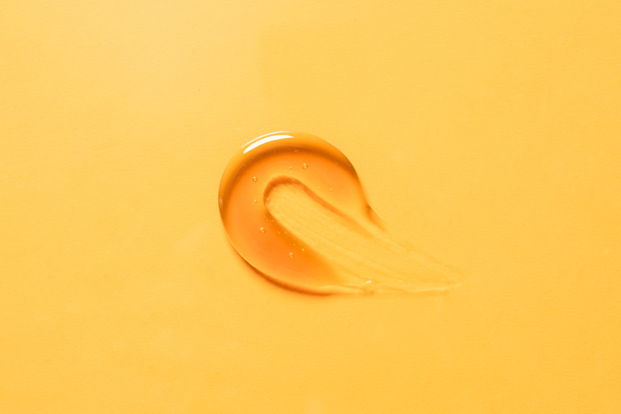 Drop of liquid collagen on a vibrant yellow surface, showcasing its smooth texture and rich hue.